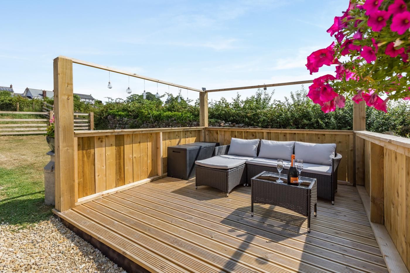 Ein Außenbereich mit einer Holzterrasse, einer Sofagruppe und einem Tisch mit Flasche und Gläsern.