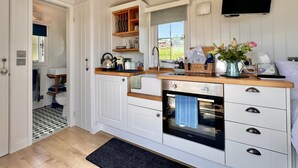 Ett kompakt kök med vita skåp, en inbyggd ugn och ett fönster med utsikt över ett grönskande landskap.