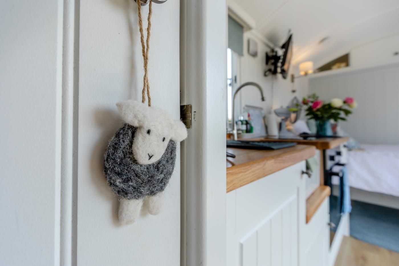 Un interior acogedor con una puerta blanca, una decoración de oveja colgante, una encimera de madera y una cama con cubierta azul.