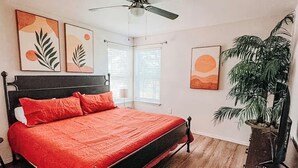 Un dormitorio con cama, ventilador de techo, ventana y una planta.