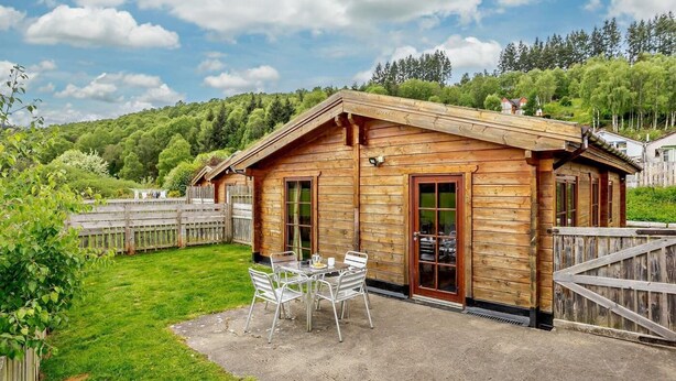 Eine Holzhütte mit einer Terrasse, einem Tisch mit Stühlen und einem Holzzaun.