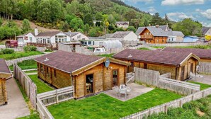 Ein ländliches Dorf mit Holzhäusern, einem grasbewachsenen Innenhof und einer Hügelkulisse im Hintergrund.