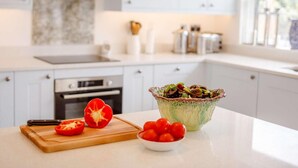 Een keuken met een marmeren spatwand, een snijplank met een halve rode paprika, een saladeschaal en een schaal met cherrytomaten.