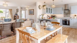 Een moderne keuken met lichtblauwe kastjes, een centraal eiland en een eethoek met een houten tafel en stoelen.