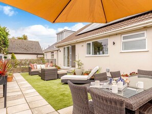 Un espace patio aménagé avec du mobilier d’extérieur, une table sur laquelle sont disposés divers objets et un grand parasol.