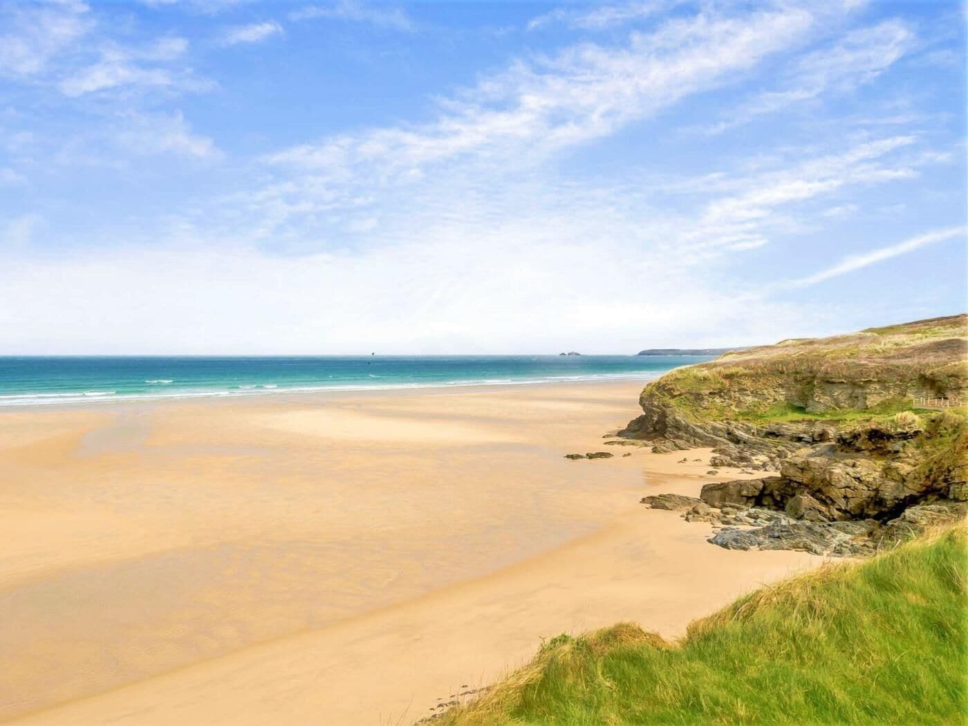 A beach with a clear sky, a sandy shore, and rocky cliffs.