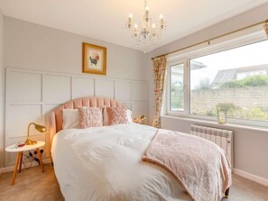 Une chambre à coucher avec un grand lit, un lustre, une table de chevet avec une lampe et une fenêtre avec des rideaux.