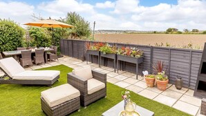 Een terras met tuinmeubilair, een tafel met een karaf en bloembakken.