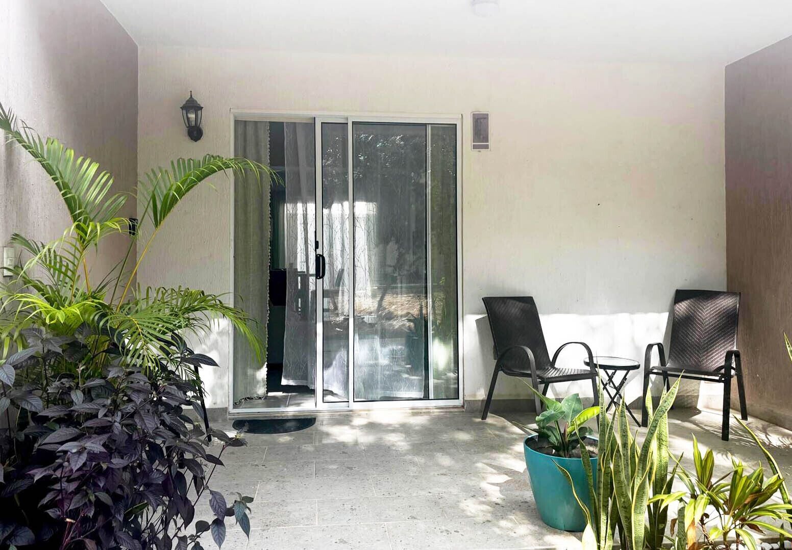 A balcony with a sliding glass door, two chairs, and various potted plants.