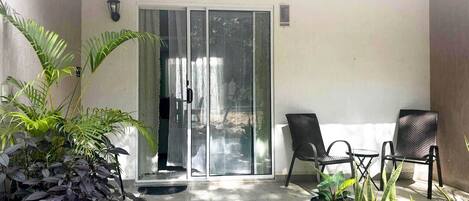 A balcony with a sliding glass door, two chairs, and various potted plants.