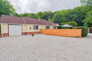 Einbungalow mit Garage, einem Schotterweg und einem Holzzaun.