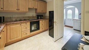 A kitchen with wooden cabinets, a black oven, a stainless steel refrigerator, and a dining area with a table set for two. - 1 Bed in Winterborne Zelston (oc-r43274) (Winterborne Zelston)