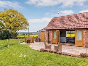 Ein rustikales Haus mit Ziegeldach, einer Terrasse mit Korbmöbeln und Blick auf ein Feld.