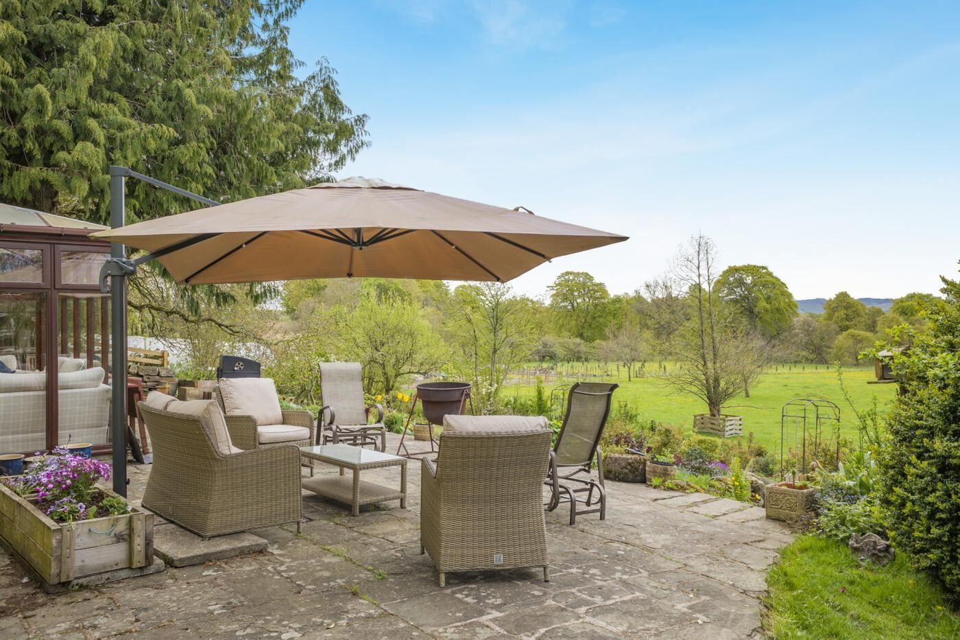 A patio with wicker furniture, a large umbrella, and a view of a green field.