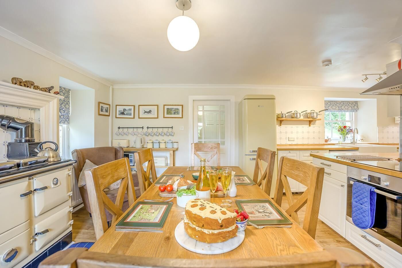 A dining area with a wooden table, chairs, a cake, and a kitchen in the background.