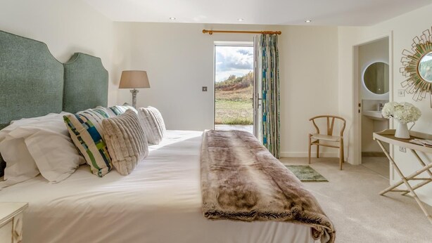Ein Schlafzimmer mit Bett, Sessel, Schreibtisch, Lampe und Blick ins Freie.