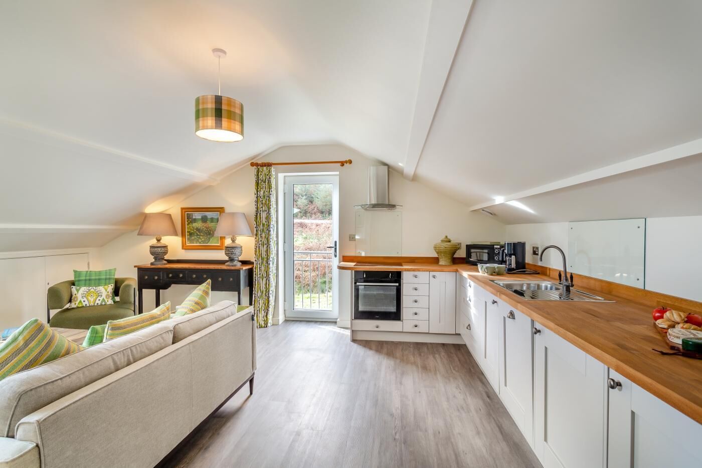 Un accogliente loft con angolo cottura, un divano con cuscini decorati, un tavolo da pranzo e vista su una zona esterna tramite una porta in vetro.