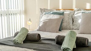 Ein ordentlich gemachtes Bett mit aufgerollten Handtüchern, einer Nachttischlampe und gemusterten Kissen.