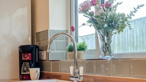 Eine Küche mit einem modernen Wasserhahn, einer Kaffeemaschine und einem Fenster mit Blick auf einen Zaun.