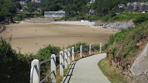 Ein Küstenweg, der zu einem Sandstrand führt, mit Blick auf ein Gebäude im Hintergrund.