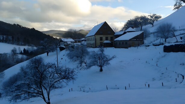 A snow-covered landscape with a large building, possibly a hotel, surrounded by trees and hills.