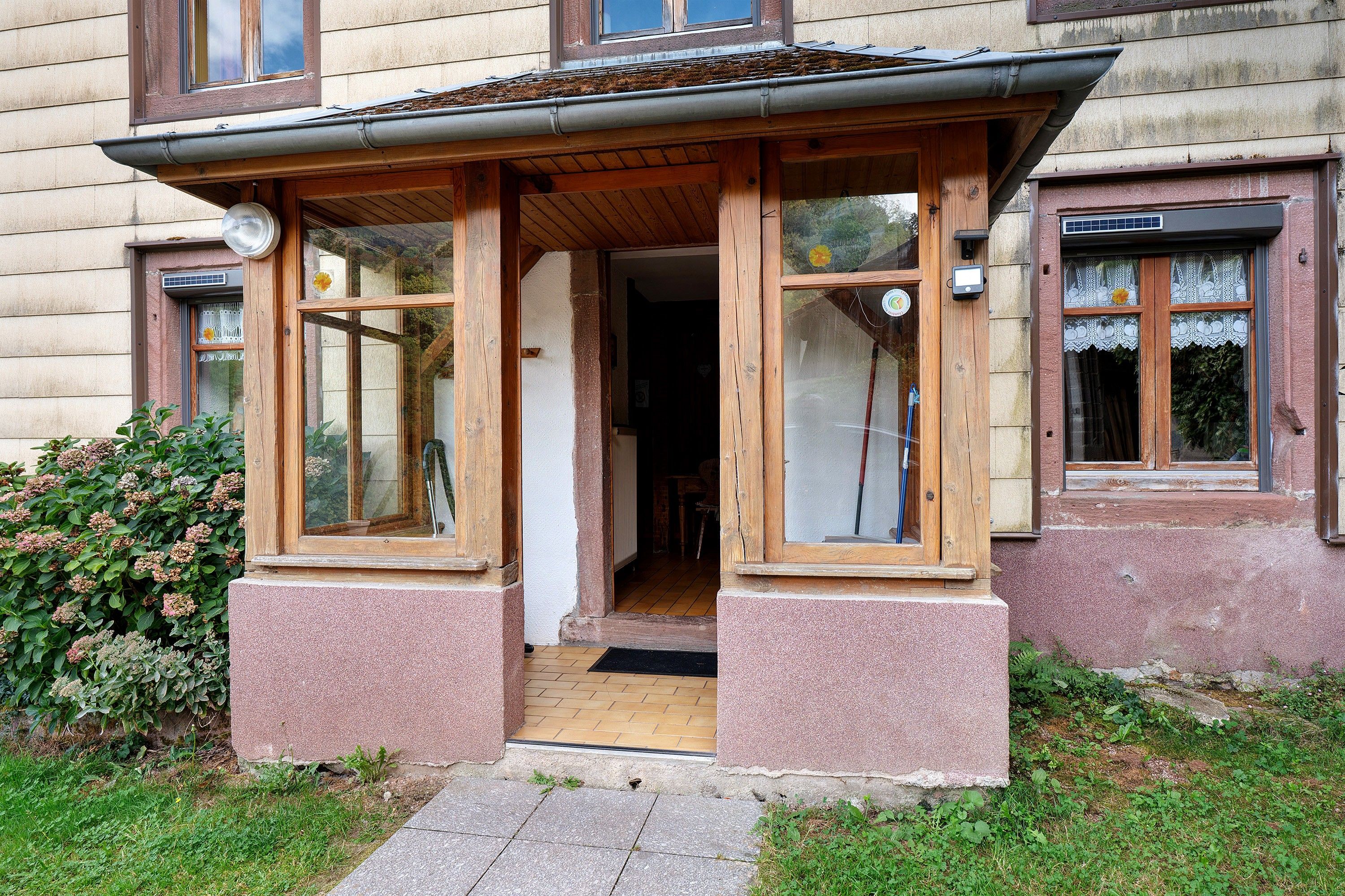 Een gebouw met een houten veranda, grote ramen en een deur die naar de binnenruimte leidt.