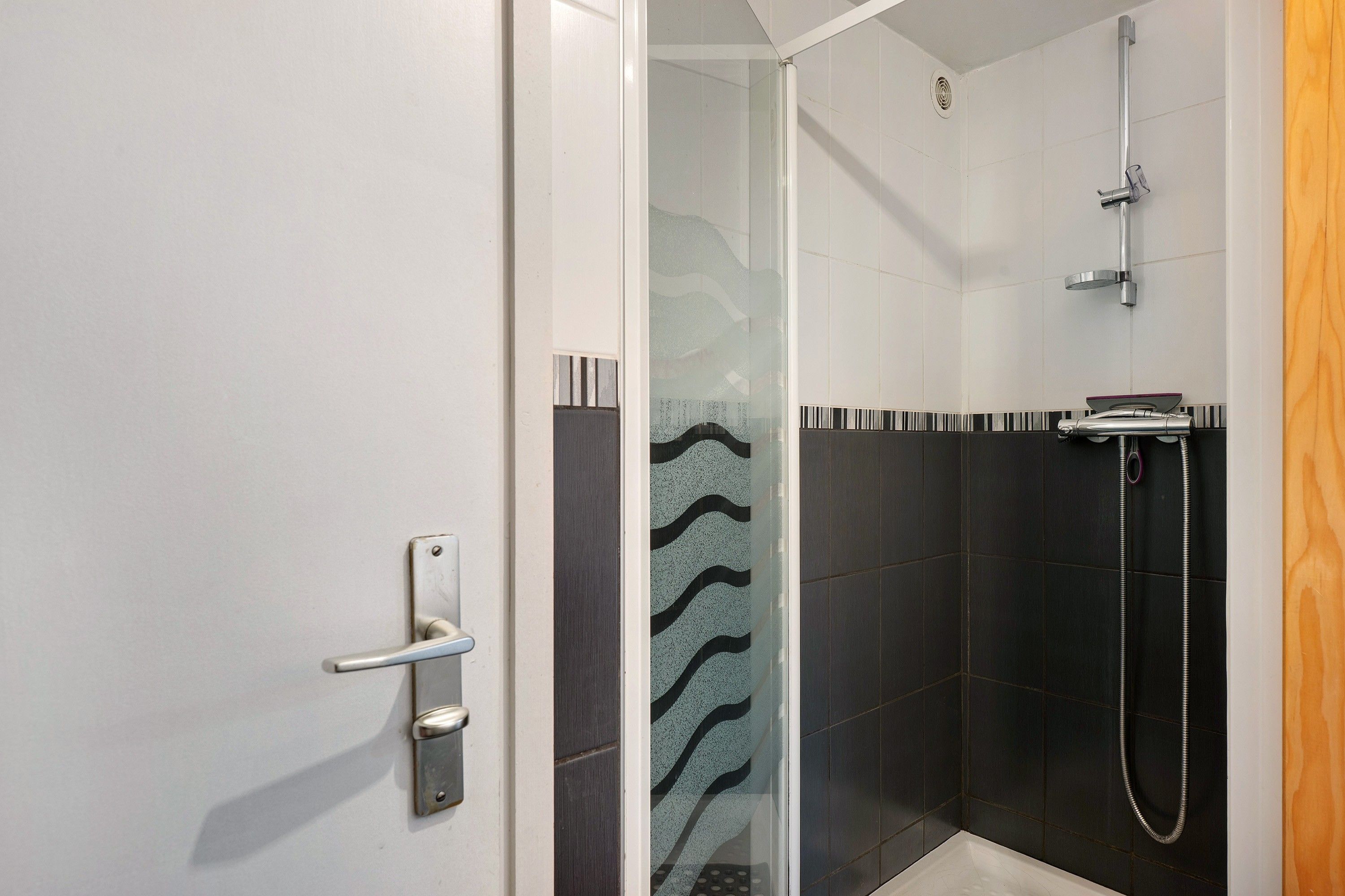 Un área de ducha con puerta de vidrio, cabezal de ducha y pasamanos.