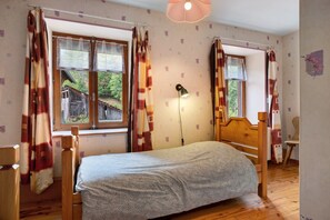 A bedroom with a bed, wooden headboard, a nightstand, a lamp, and curtains.