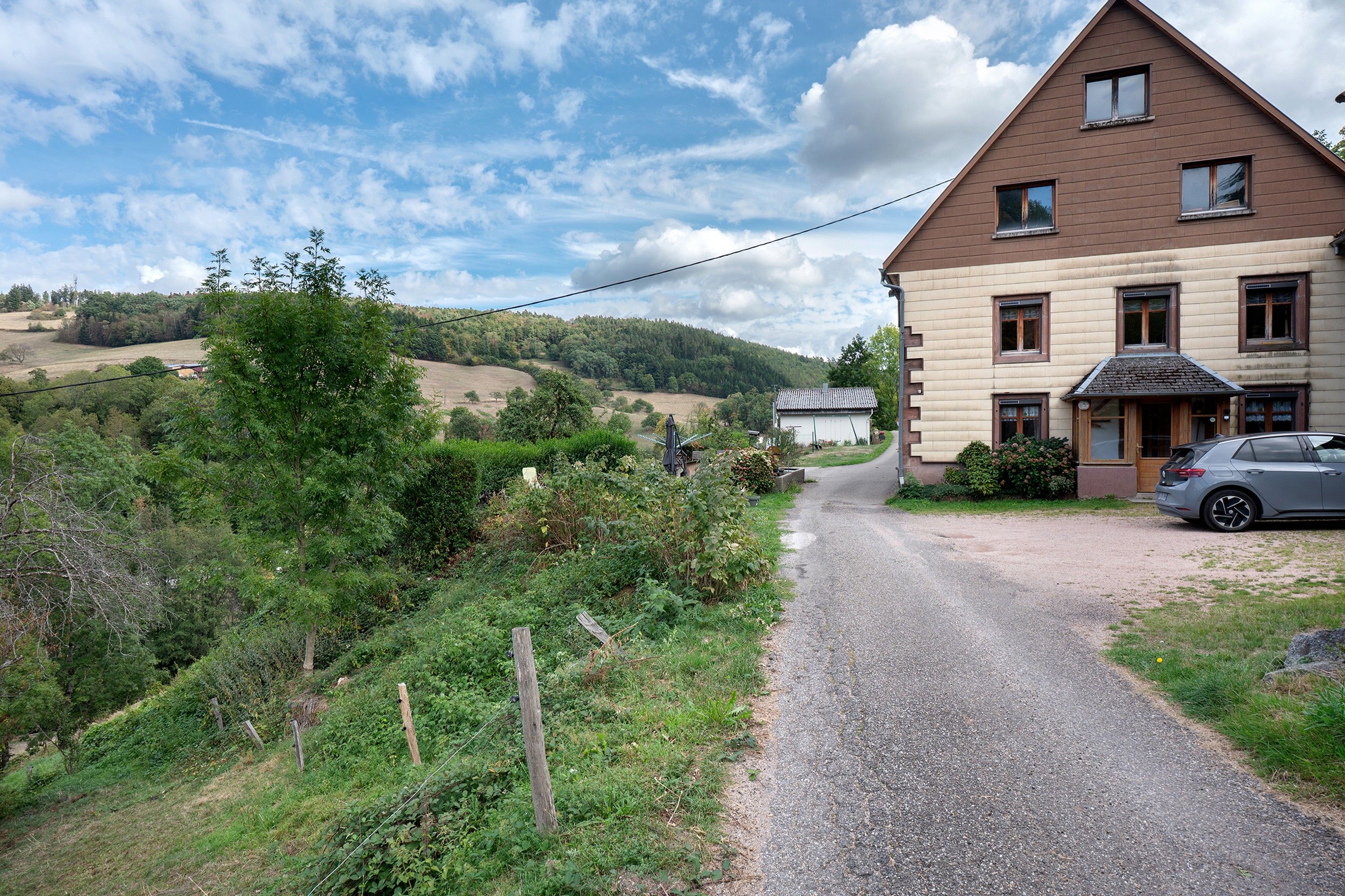 Een landweg die naar een tweegevelwoning leidt, met een auto op de oprit.