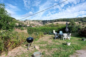 A garden with a barbecue grill, outdoor table and chairs, and a view of rolling hills in the background. - Gîte les hambostures (Lapoutroie)