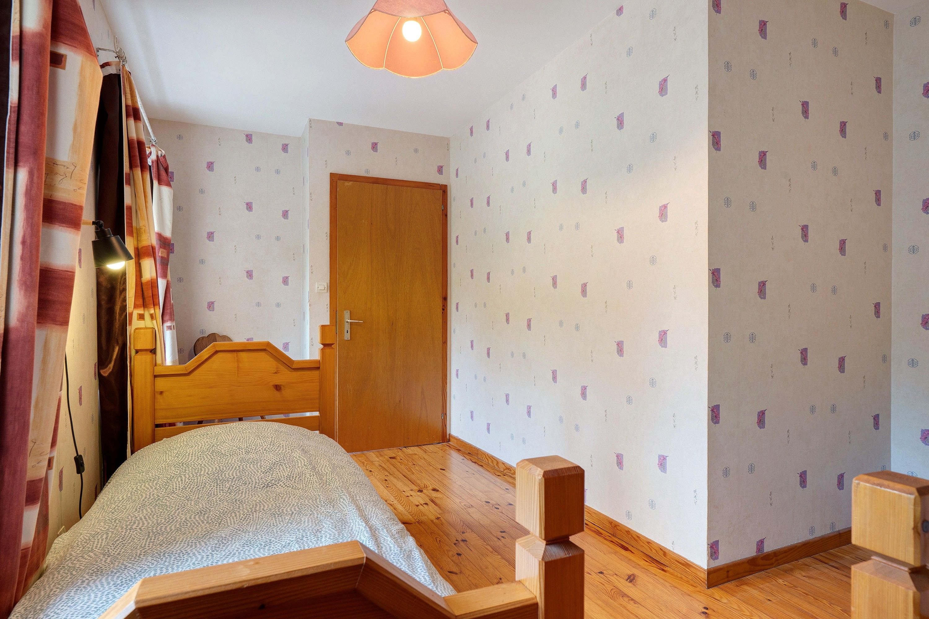 Une chambre à coucher avec un lit en bois, une porte et un papier peint à motifs.