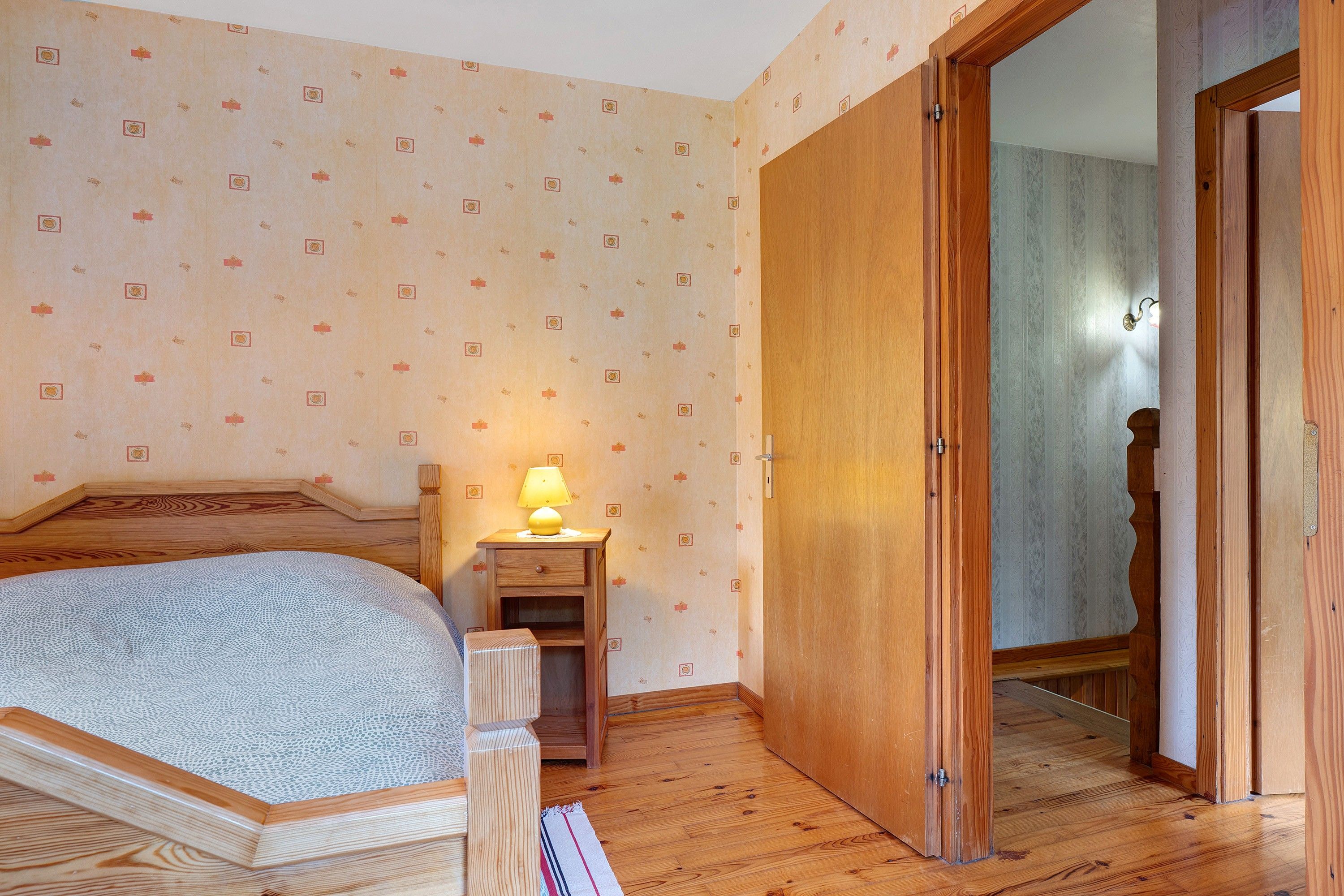 Un dormitorio con una cama, una mesita de noche con lámpara, un armario de madera y un espejo.