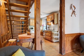 A rustic interior with a wooden staircase, a dining area, and kitchen cabinets. - Gîte les hambostures (Lapoutroie)