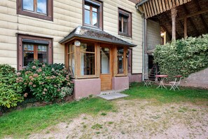 A traditional wooden house with a porch, a small garden, and a gravel pathway leading to the entrance.