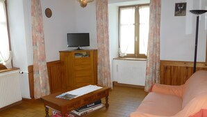 A room with a wooden floor, a sofa, a wooden cabinet with a television, and a radiator.