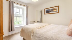 Ein Schlafzimmer mit großem Fenster, einem Bett mit weißer Bettdecke, einem gerahmten Bild an der Wand und Holzboden.
