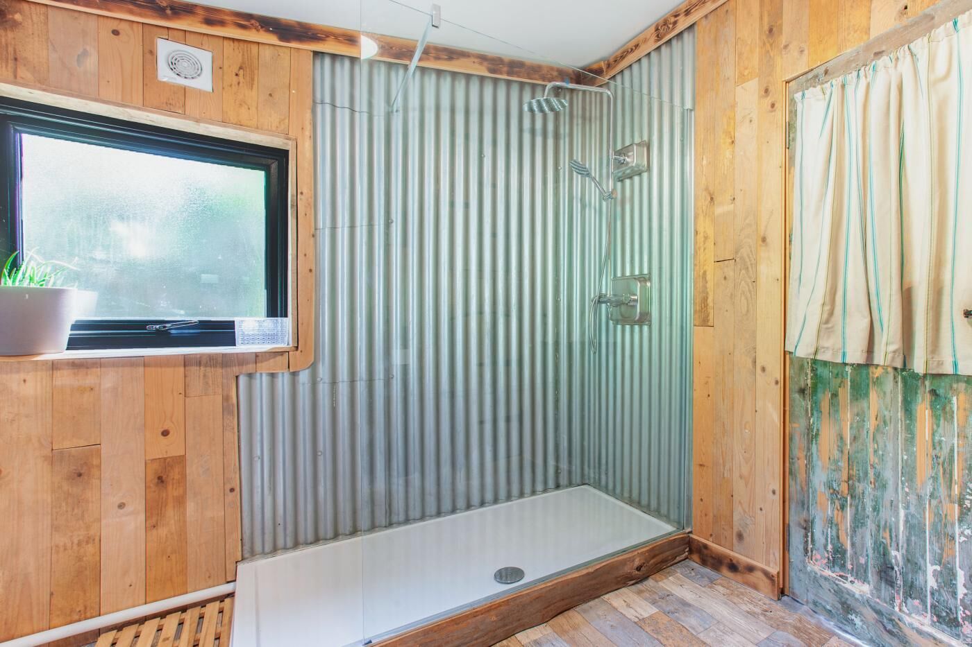 Un intérieur en bois avec une douche, une fenêtre et un rideau.