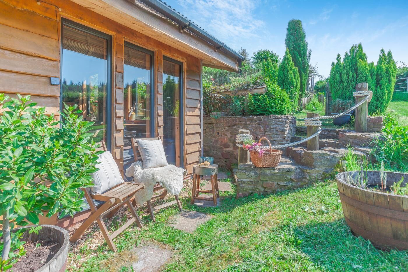 Uma cabana de madeira com um alpendre, móveis de exterior, uma parede de pedra e um jardim.