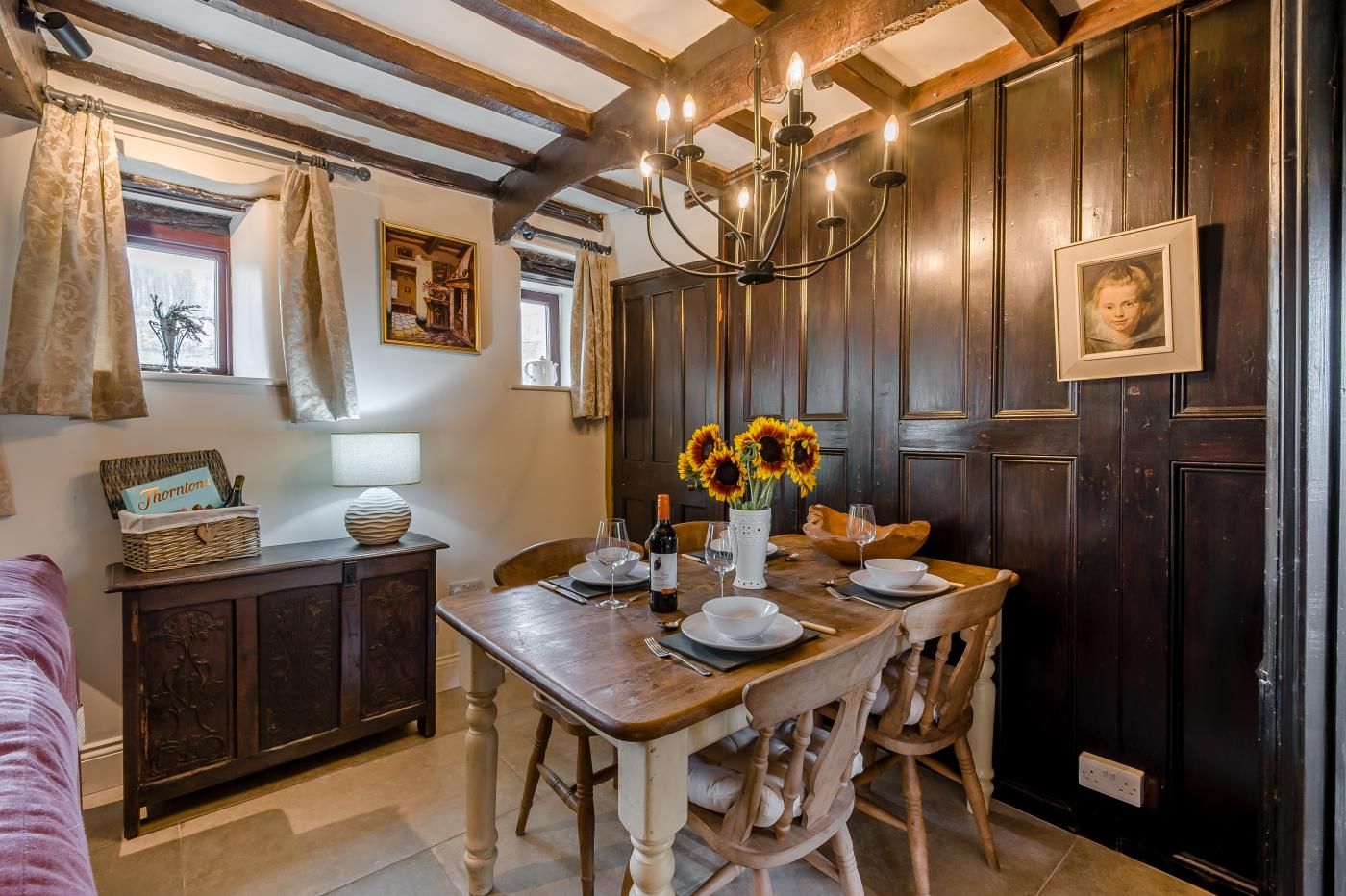 A dining area with a wooden table set for two, a chandelier, and a vase with sunflowers.