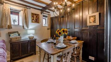 A dining area with a wooden table set for two, a chandelier, and a vase with sunflowers.