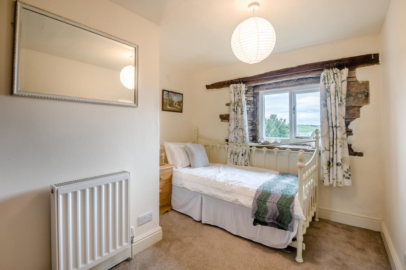 A bedroom with a bed, a radiator, a window with curtains, and a hanging light fixture.