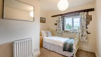 A bedroom with a bed, a radiator, a window with curtains, and a hanging light fixture.