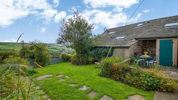 A rustic stone house with a green door, a garden with a stone path, and a view of the countryside.