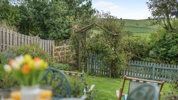 A garden with a wooden fence, a pergola with climbing plants, and a table with chairs in the foreground.