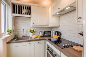 A modern kitchen with white cabinets, a built-in microwave, a stovetop, and a window with a plant. - 2 Bed in Bradley (oc-w44709) (Skipton)