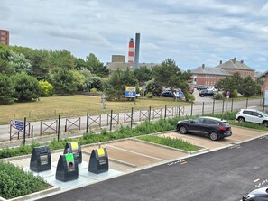 Ein Parkplatz mit markierten Stellplätzen, einem Wertstoffcontainer und einem Fußgängerüberweg-Schild.