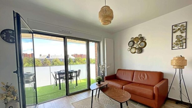 Un salon moderne avec un canapé en cuir marron, une petite table et un lampadaire. Une grande fenêtre offre une vue sur une pelouse verdoyante et des immeubles.