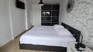 Une chambre à coucher avec un lit, une table de chevet, une lampe et un mur orné d’un motif floral.