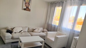 A living room with a sofa, a coffee table, and a chair. There is a radiator and a window with curtains. - Just a short walk from Avignon's historic center, a quiet apartment, (Avignon)