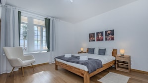 A bedroom with a wooden bed, a chair, a window with curtains, and wall art. - GuestReady - Doctor House Gardens (Horta)